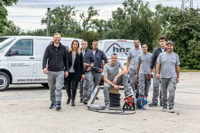 Team eines Elektrobetriebs mit Firmenfahrzeugen und Werkzeug