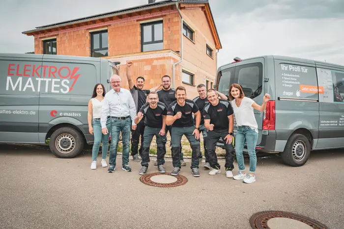 Betriebsteam mit Büro- und Montagemitarbeitern vor den Firmenfahrzeugen